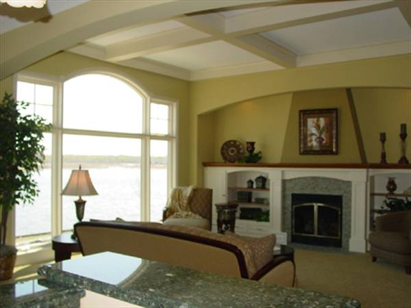 Living room with brown seats, glass-enclosed fireplace, coffered ceiling, and clerestory windows overlooking the breathtaking lake view.
