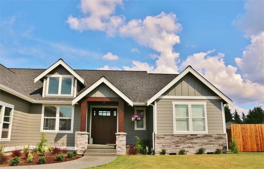 Front exterior view showing the covered porch, gray siding, stone accents, and a large dormer window.