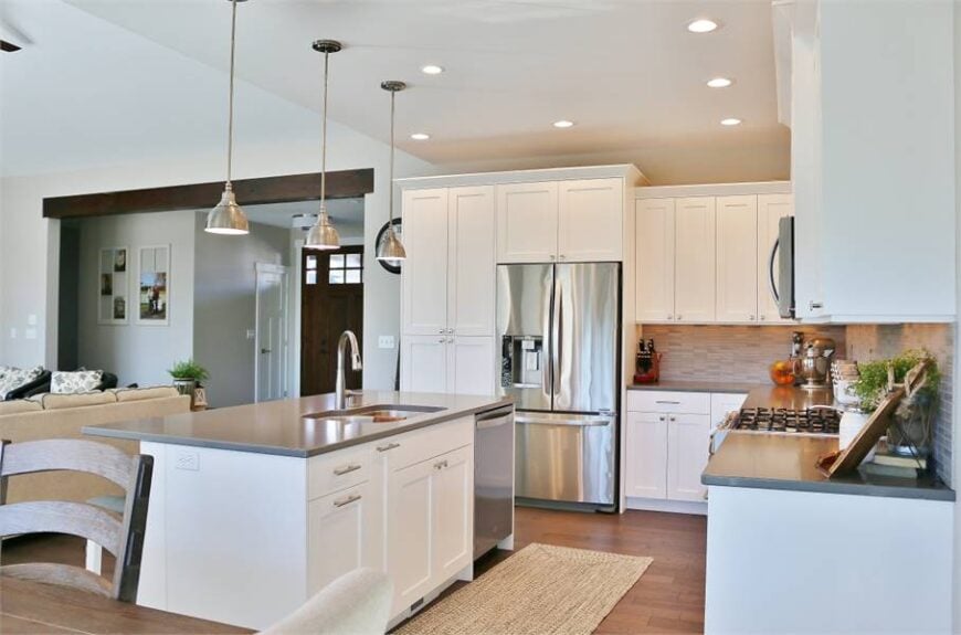 The kitchen is equipped with stainless steel appliances, white cabinetry, and a double bowl sink fitted on the center island.