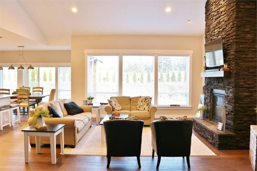 Living room with beige seats, wooden tables, patterned area rug, and a stone fireplace with a TV on top.