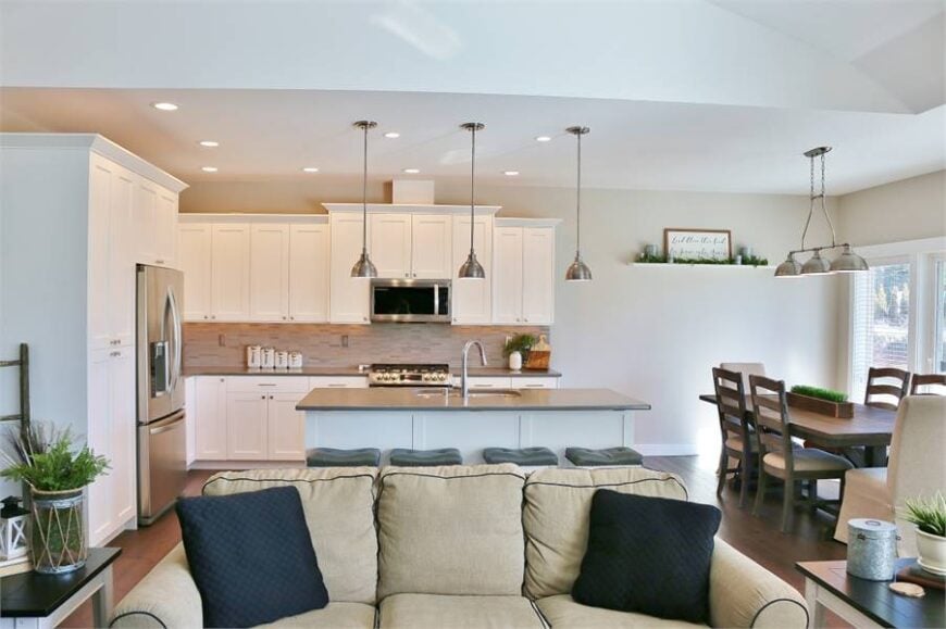 The kitchen sits behind the beige sectional that's accentuated with black throw pillows.