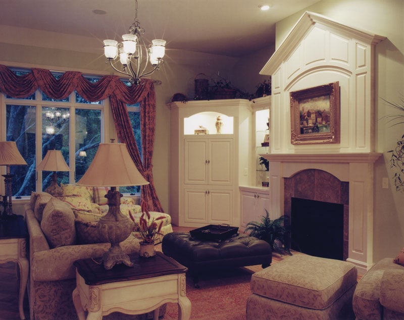 The living room has patterned seats, leather tufted ottoman, fireplace, and clawfoot tables topped with classic table lamps.