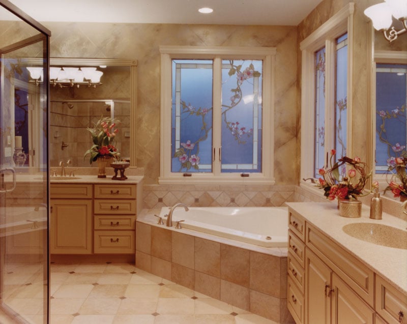 The primary bathroom offers his and her vanities, a corner tub, and a walk-in shower reflected in the mirror.