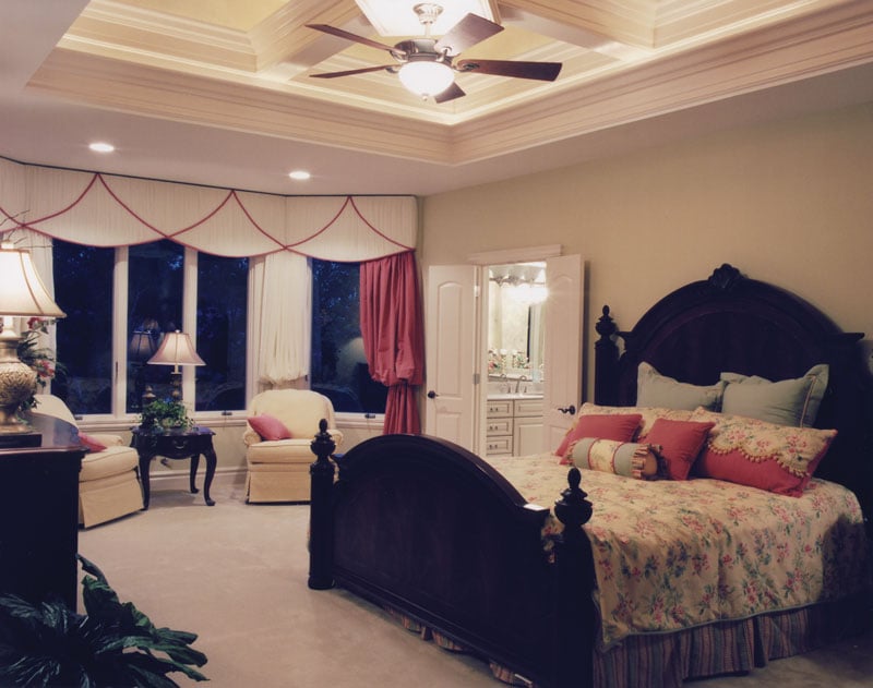 The primary bedroom has dark wood furnishings, a coffered ceiling, and a sitting area by the bay window.
