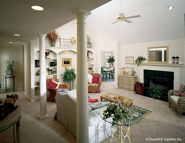 Living room with skirted sofa, cushioned armchairs, arched built-ins, and a fireplace with a mirror on top.
