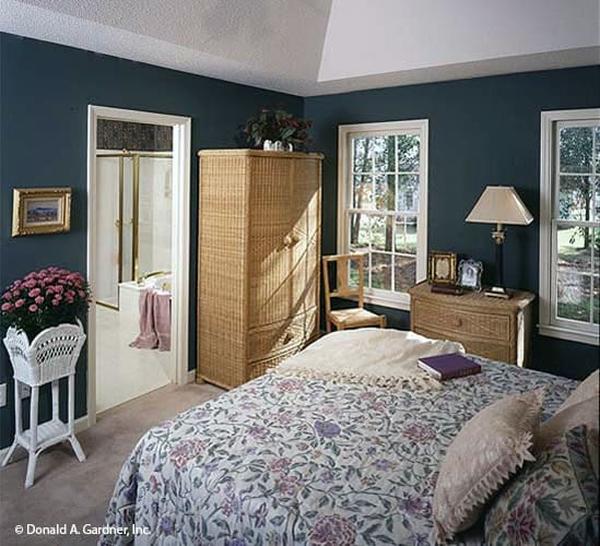The primary bedroom has a cozy bed, wicker dressers, blue walls, and a high coved ceiling.