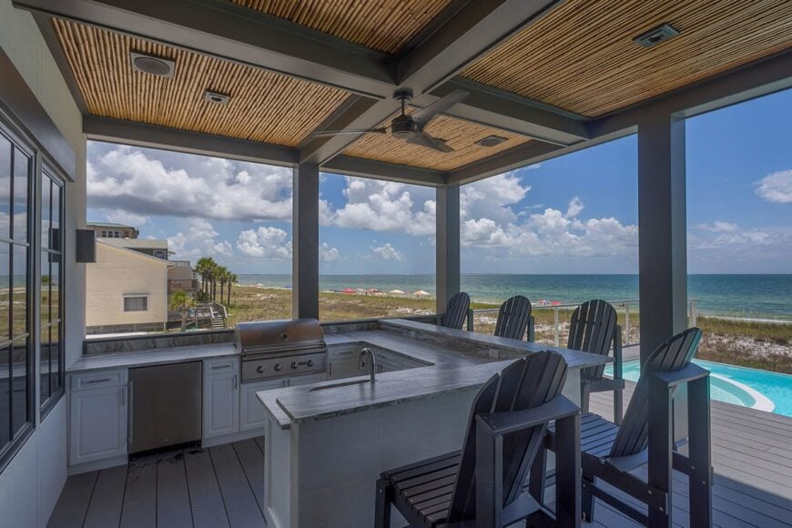 Covered deck filled with a summer kitchen and gray counter chairs.