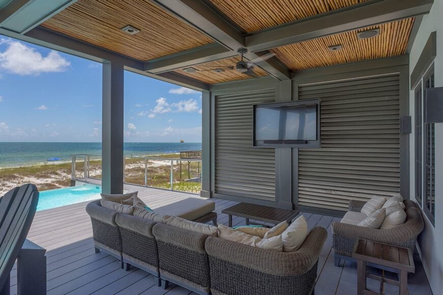 Wicker chairs, wooden coffee table, and a wall-mounted TV complete the covered deck.