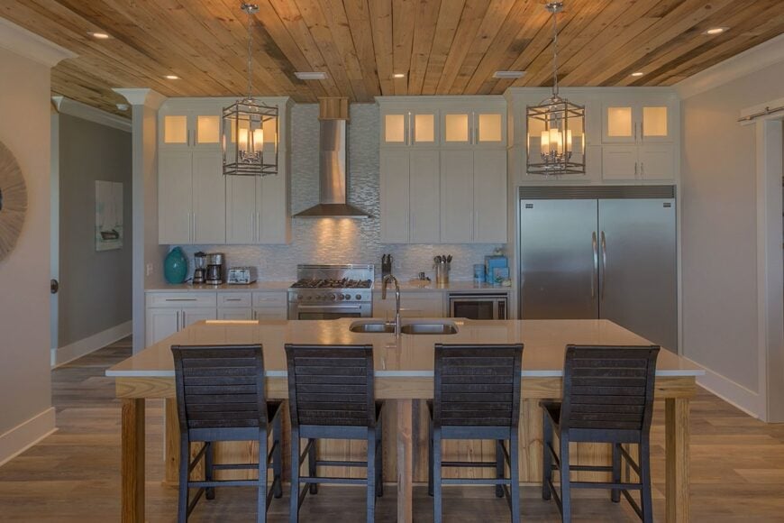 The kitchen has white cabinetry, slate appliances, and breakfast island well-lit by a pair of caged pendants.