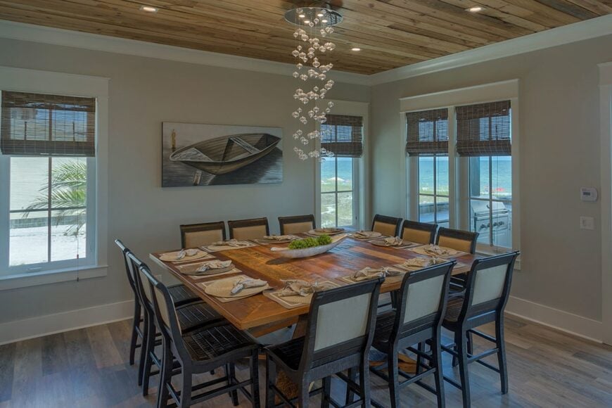 The dining room has a cascading chandelier, boat artwork, and a large wooden table surrounded by matching chairs.