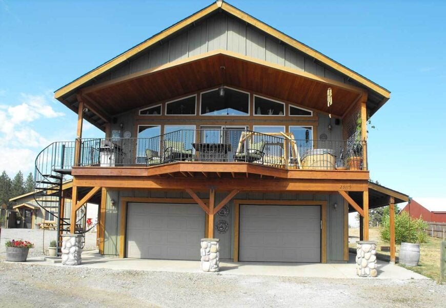 Front exterior view with a double garage and a wide covered deck enclosed in wrought iron railings.