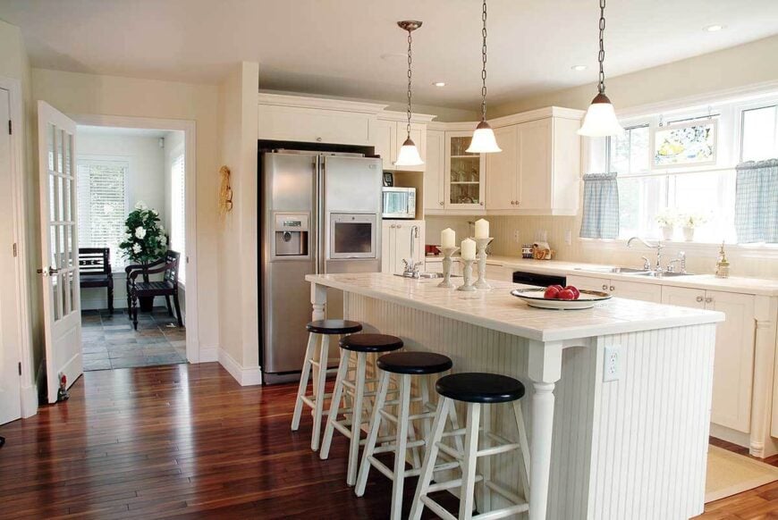The kitchen has white cabinets, stainless steel appliances, and a beadboard island lined with round bar stools.