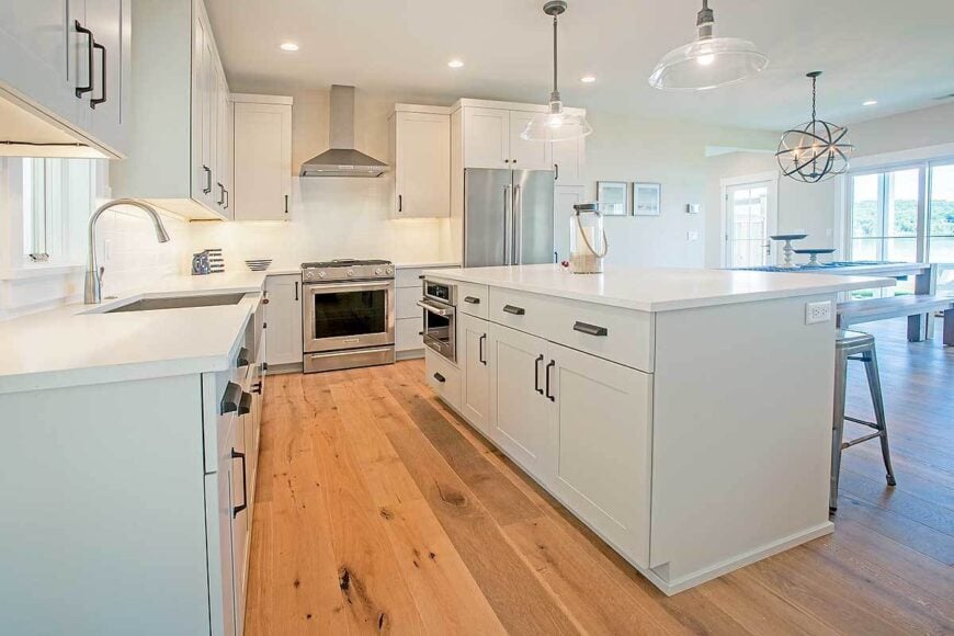 Kitchen with white cabinetry, stainless steel appliances, quartz countertops, and glass dome pendants.