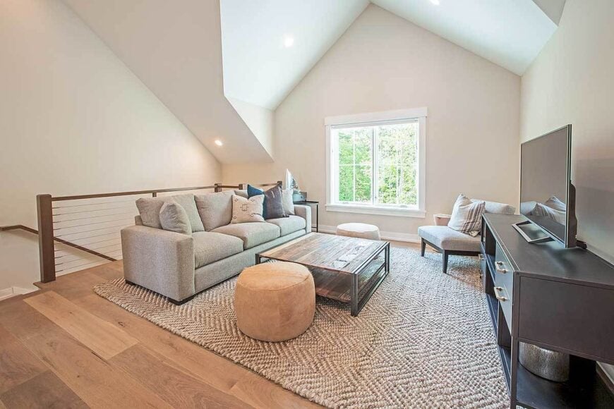The loft is filled with gray sectional and chair, wooden coffee tables, velvet ottomans, and a flatscreen TV.