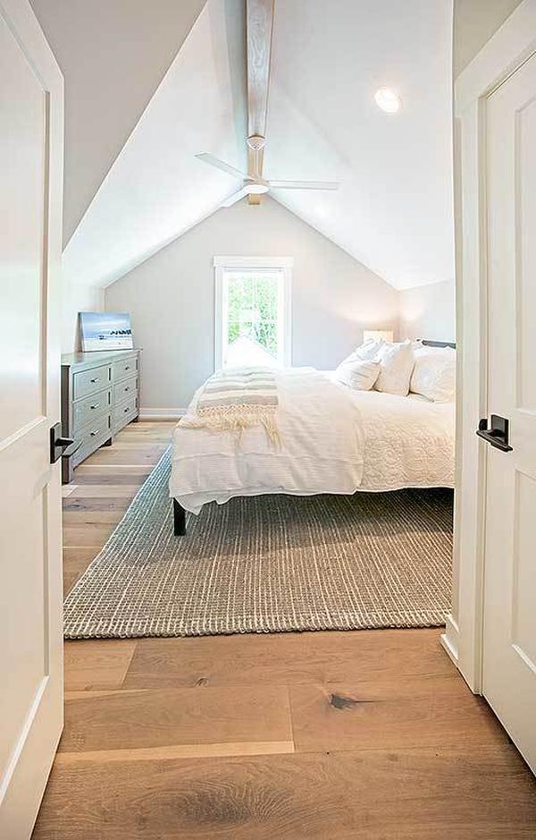 This bedroom has dark wood furnishings, a vaulted ceiling, and wide plank flooring topped by a jute area rug.
