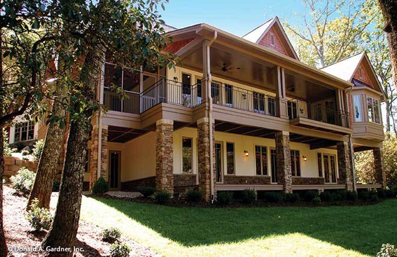 Rear exterior view with expansive patio and balcony supported by stone columns.