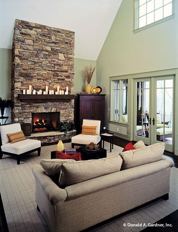The living room has a gray sofa, white cushioned chairs, a stone fireplace, and a french door that leads out to the covered porch.