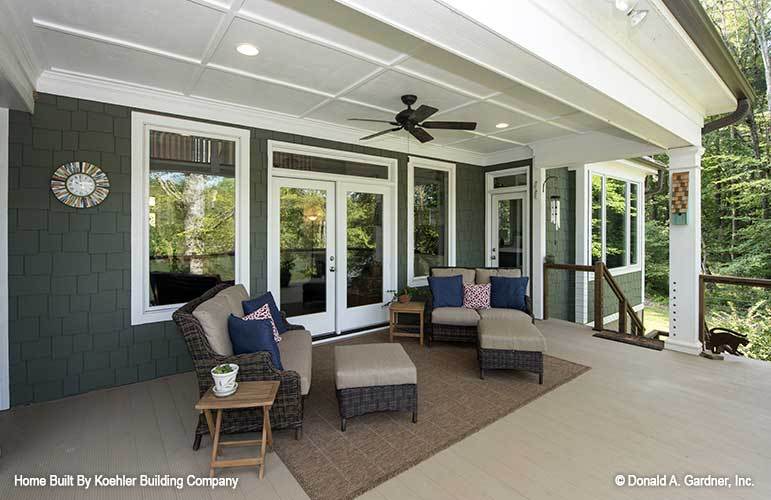 Rear porch filled with wicker seats, matching ottomans, wooden side tables, and a brown area rug.