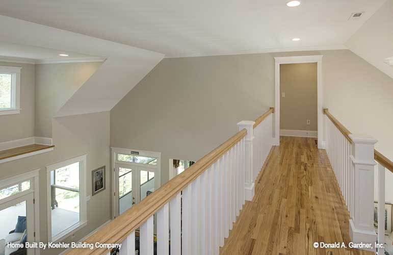 Balcony loft with vaulted ceiling, white railings, and hardwood flooring.
