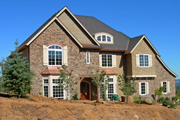 Front exterior view showing the stone cladding, gable rooflines, white-framed windows, and an arched dormer.