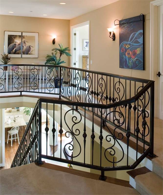 Second-floor balcony with carpet flooring, intricate railings, and beige walls accentuated with lovely artworks.