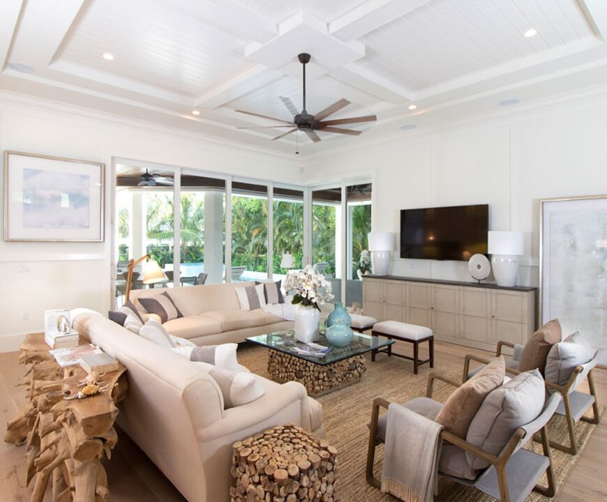 Living room with beige sectionals, cushioned seats, wall-mounted TV, and a fan hanging from the coffered ceiling.