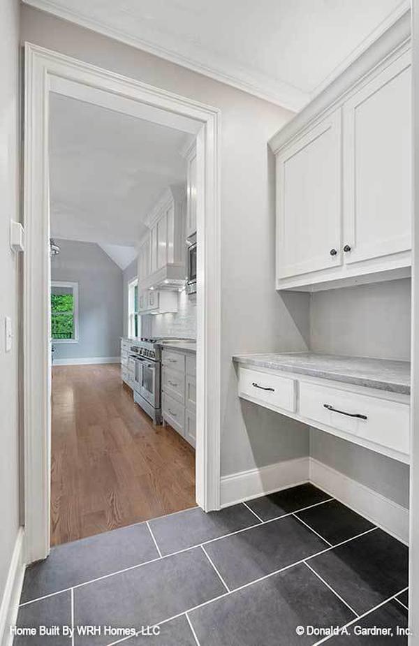 The butler's pantry has white cabinets, marble top counter, and black tiled flooring.