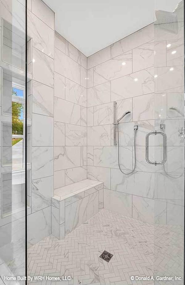 The walk-in shower has herringbone tiled flooring, marble walls, built-in seat, and chrome fixtures.