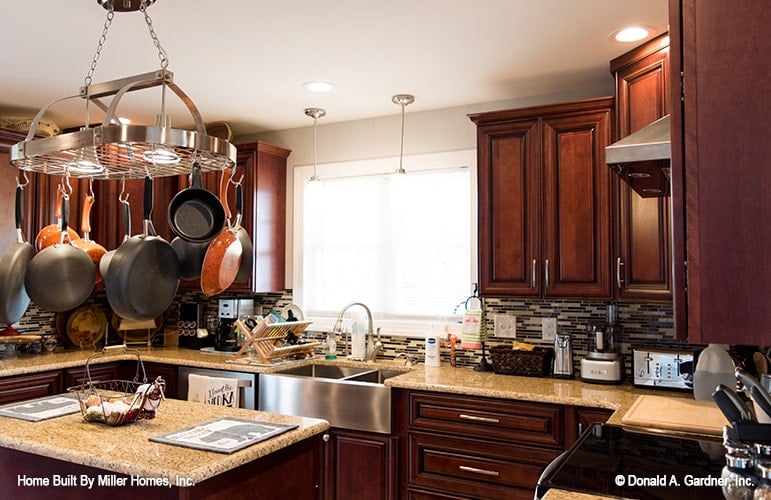 The kitchen has wooden cabinetry, a farmhouse sink, and an oval metal rack suspended above the granite top island.
