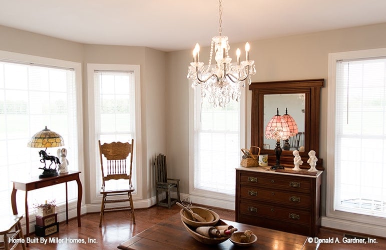 Dining room with bay window, beaded chandelier, and dark wood furnishings that blend in with the hardwood flooring.