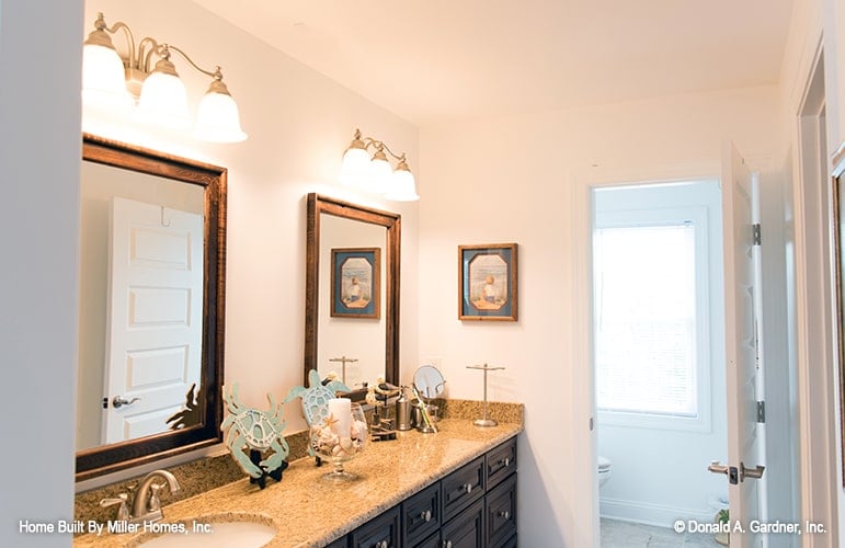 Bathroom with a toilet room and a granite top vanity paired with wooden framed mirrors.