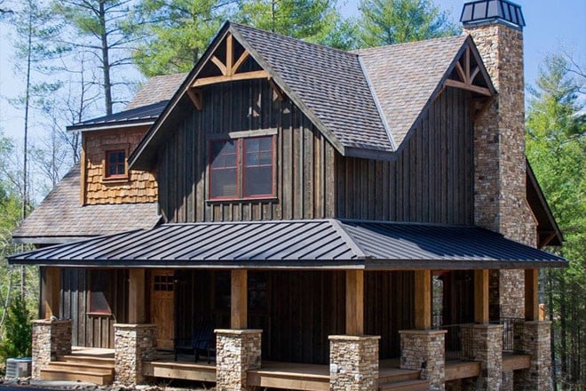 Left exterior view with a wrap-around porch, stone brick chimney, and gable roofs adorned by decorative wooden trims.