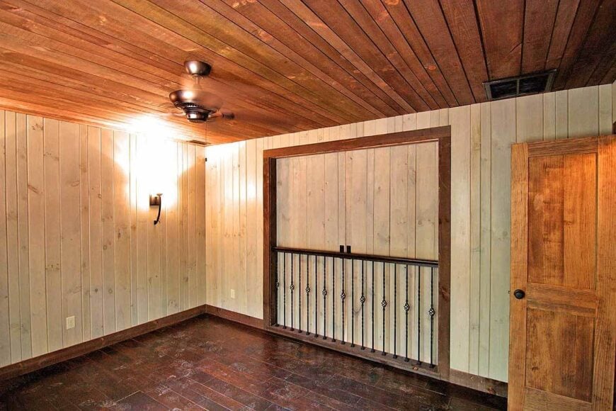 A farther view of the bedroom with closed doors, hardwood flooring, and wood-paneled walls and ceiling.