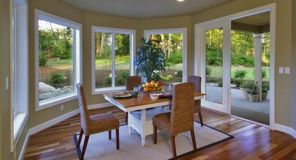 Breakfast nook with wicker chairs, wooden dining table, and a french door that leads out to the covered porch.