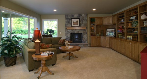 The family room has carpet flooring, a stone fireplace, green sectional, round tables, and a wide wooden built-in.