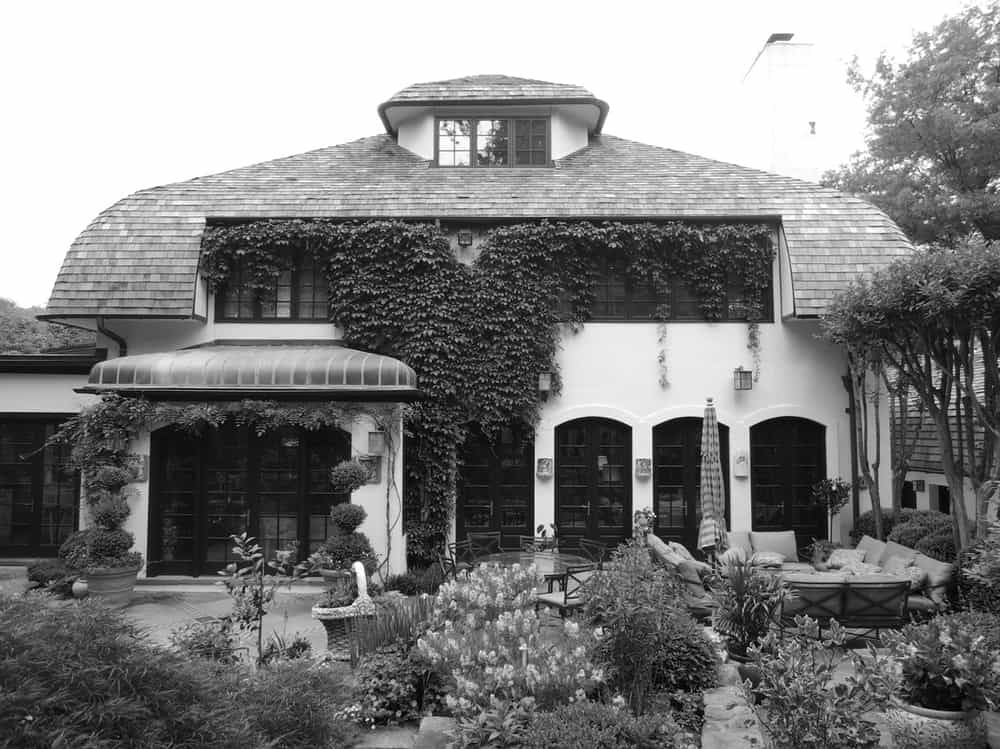 This is a black and white view of the front of the house before renovation adorned with creeping vines on its exterior walls that set a background for the sitting area.