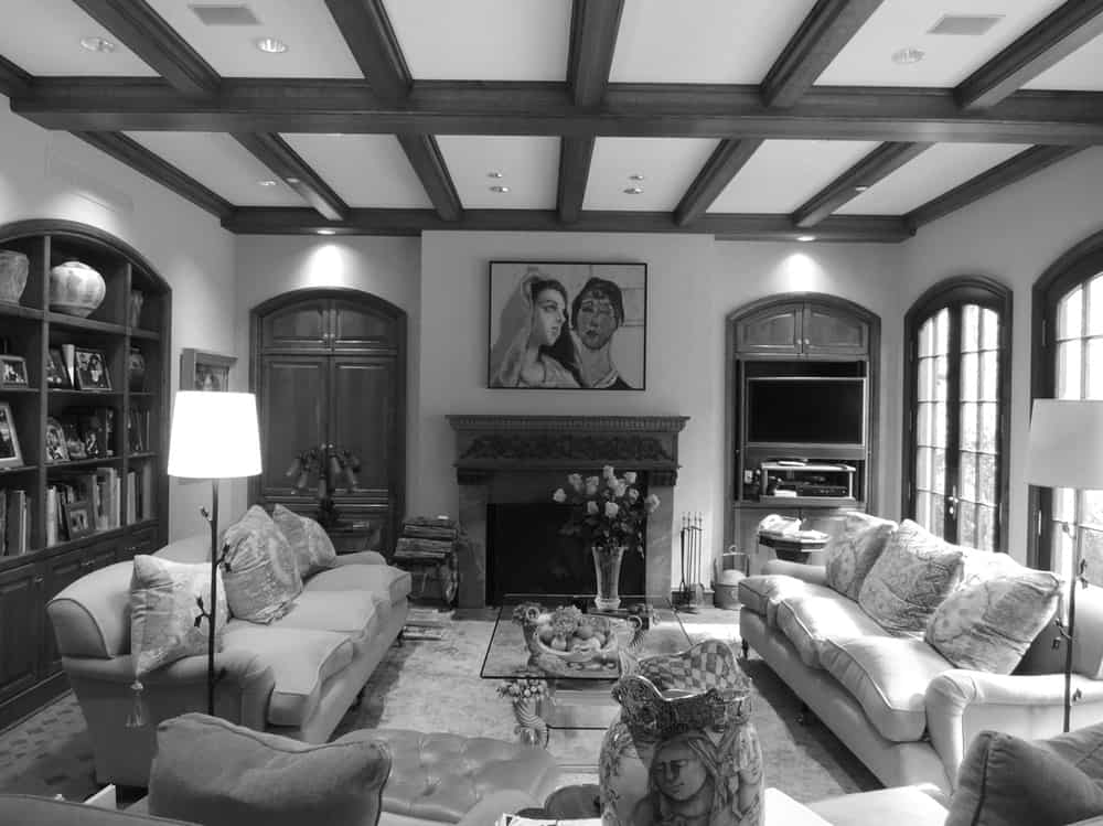 This is a black and white view of the living room of the house before renovation with a more traditional look topped with a beamed ceiling.