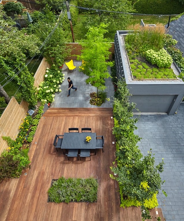 This is a look at the back of the house from the vantage of the balcony. You can see here the wooden deck floor of the patio fitted with a dark outdoor dining set surrounded by landscape of plants and flowers.