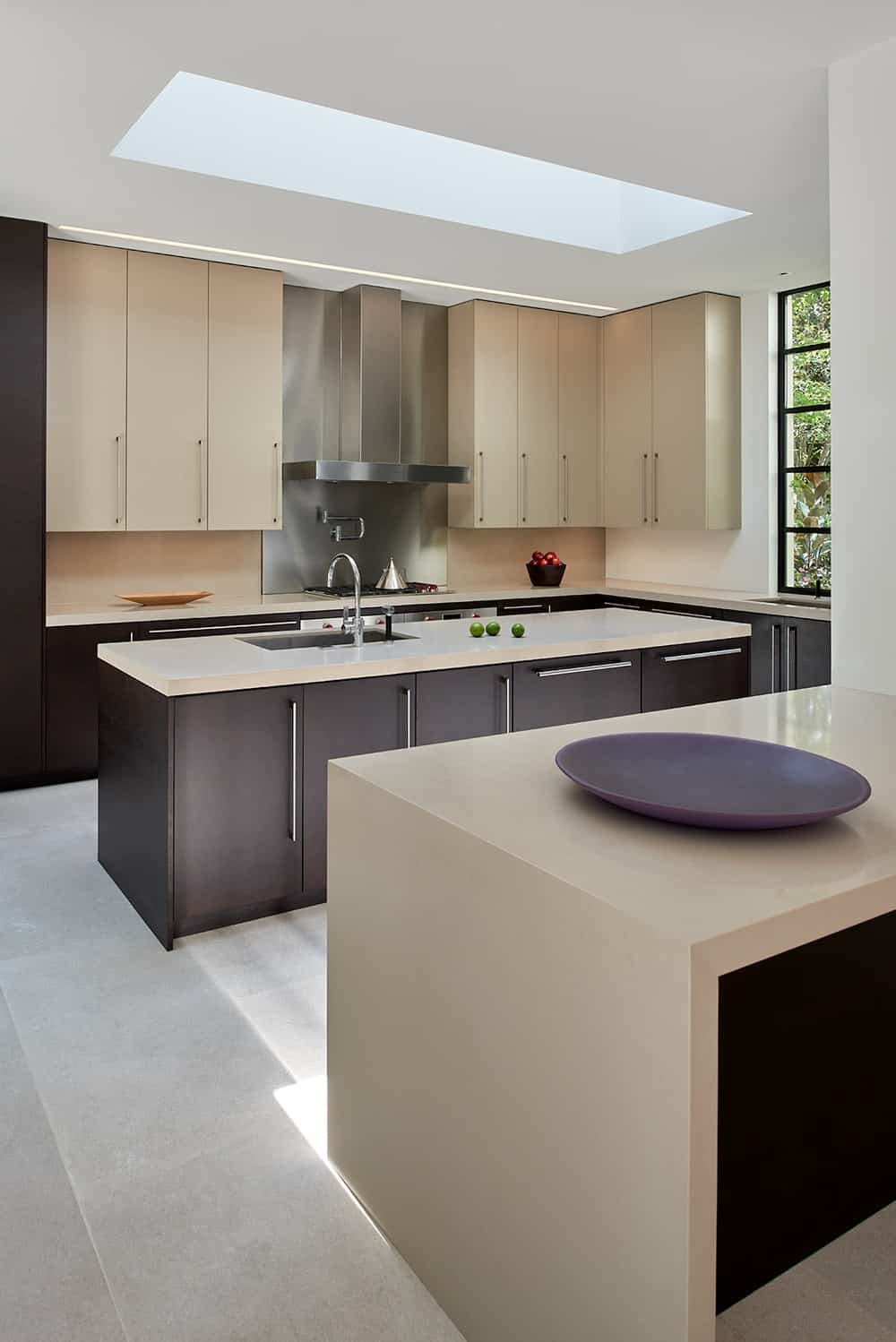 The kitchen has a beige tone to its countertops that match the dark wooden cabinetry contrasted by the bright ceiling and floor.
