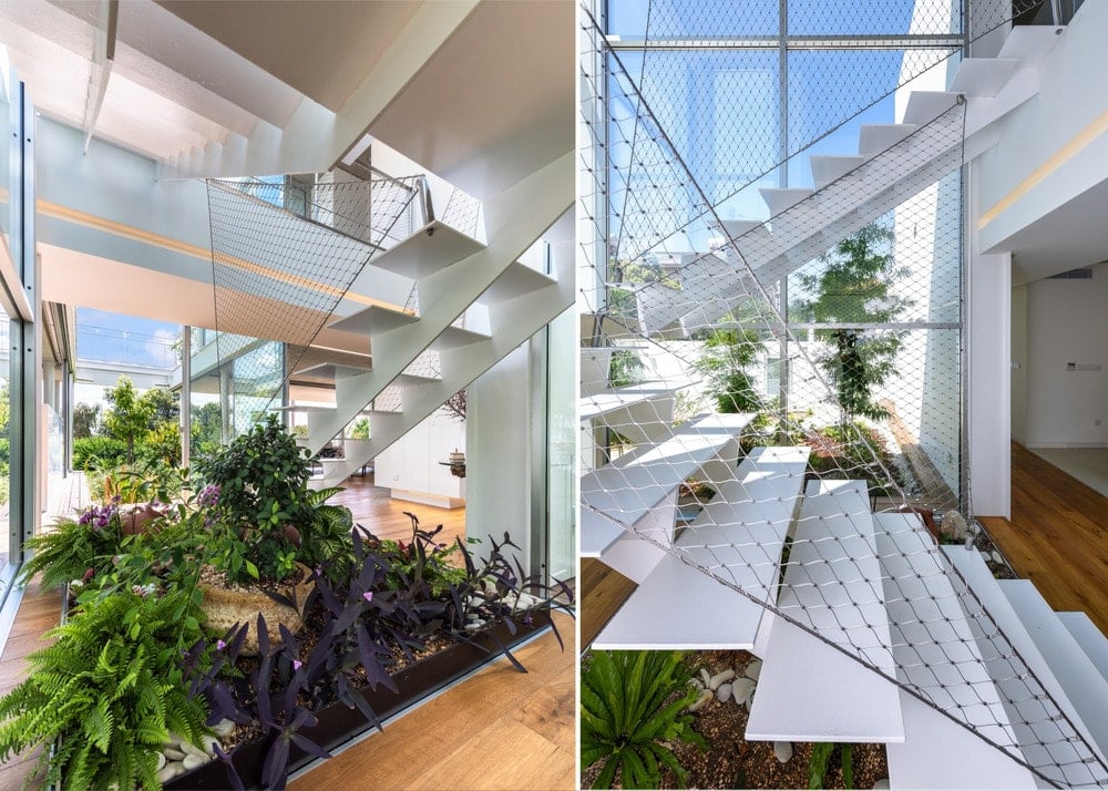 This is a close look at the modern white staircase that has net railings and adorned by plants underneath.