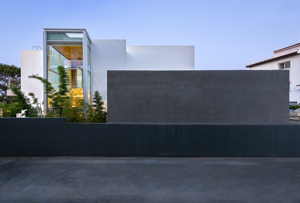 This is an exterior look of the house that has dark outer walls and white exterior walls with glass walls.