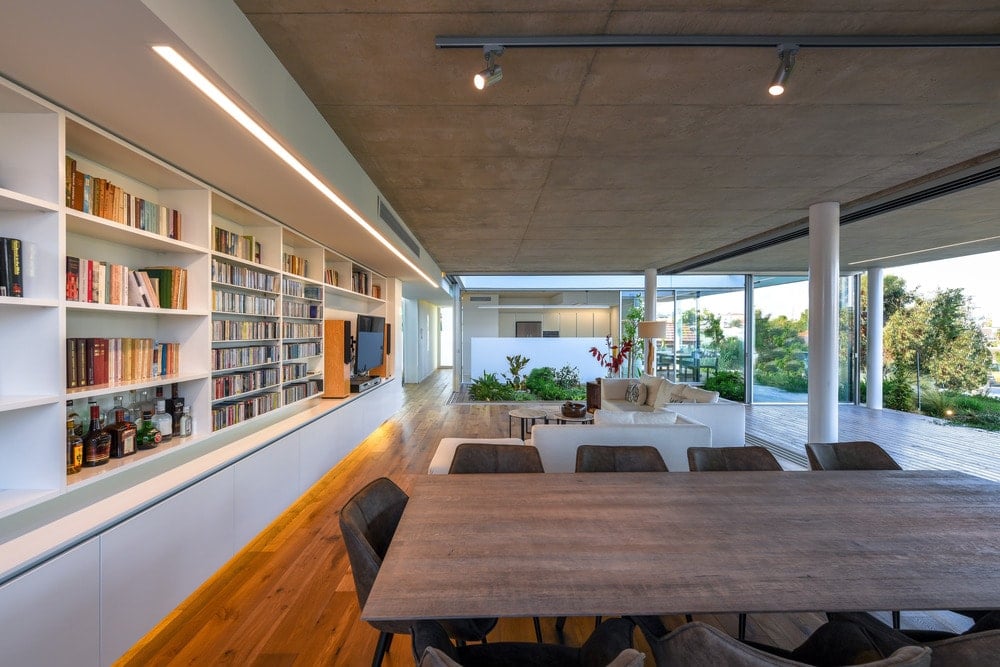 Just behind the sofa of the living room is the large table of the dining area topped with a modern lighting fixture.
