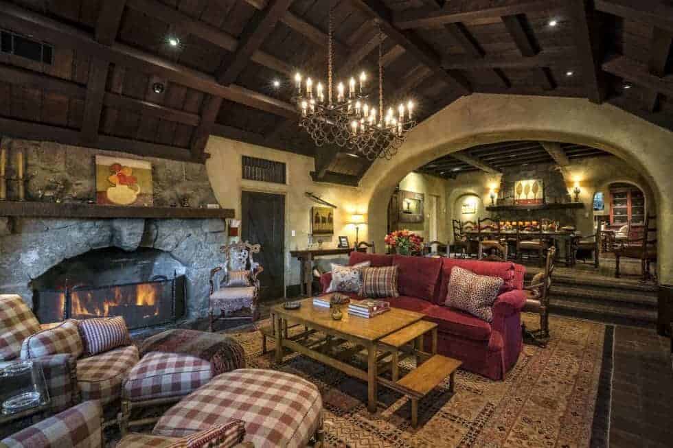 This large room houses the living room area and the dining area at the far end. The living room has a colorful sofa set flanking the wooden coffee table across from the stone fireplace. Image courtesy of Toptenrealestatedeals.com.