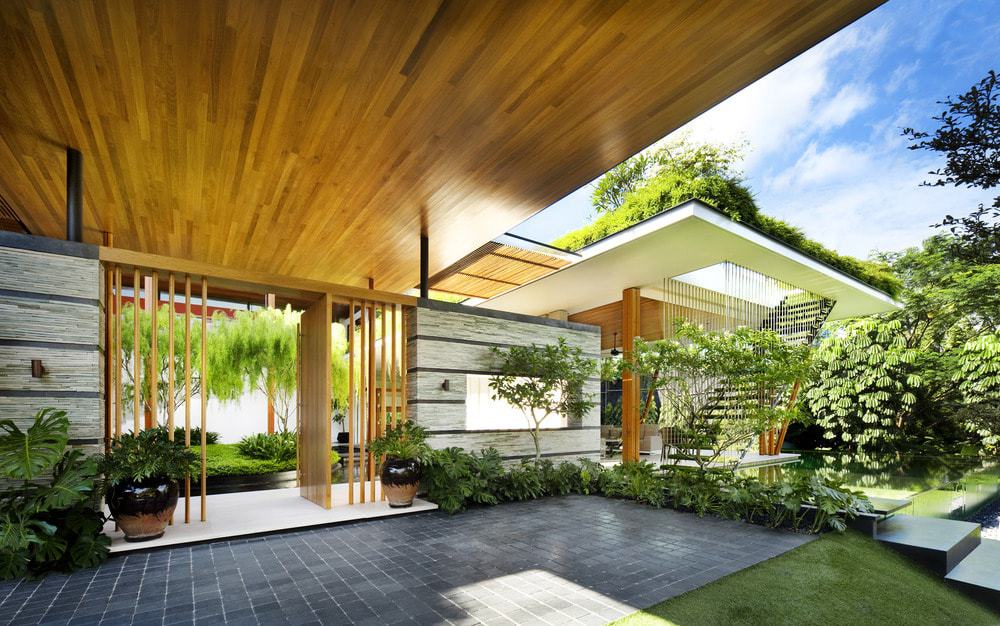 The walkway and driveway of the front area has a dark tone that is complemented by the surrounding shrubs and hanging plants.