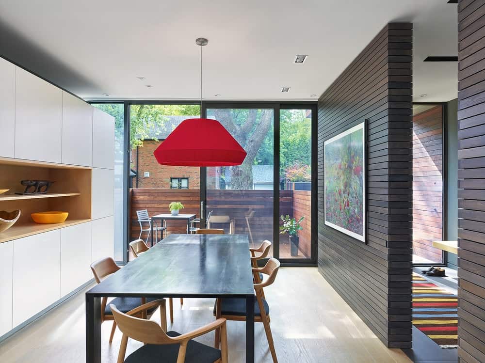 This view of the dining room showcases the red dome pendant light over the kitchen table that matches the dark wall on the side.