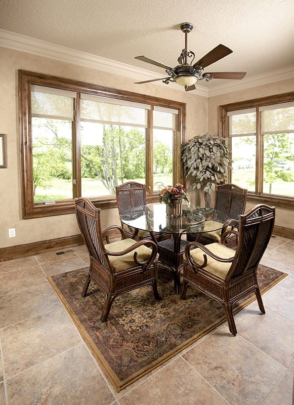 The sunroom has a ceiling fan, a glass top coffee table, and cushioned wicker chairs sitting on a classic area rug.