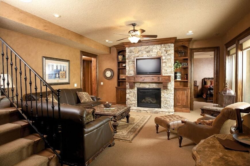 Living room with leather sofas, velvet lounge chair, carved wood coffee table, and a stone fireplace with a TV on top.