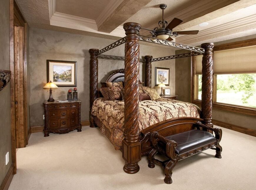 The primary suite has carpet flooring, concrete walls, carved wood nightstands, and a canopy bed with a cushioned bench at its end.