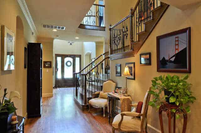 Entryway with classic chairs, wooden tables, a shelving unit, and framed artworks mounted against the staircase.