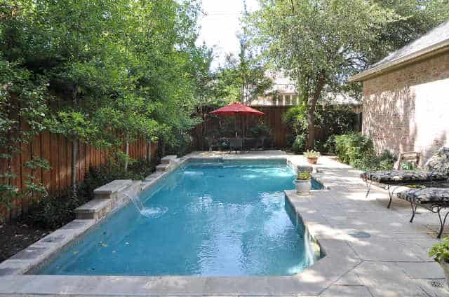 Backyard with a swimming pool surrounded by wooden fence and lush plants.